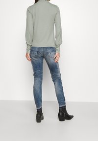 Světle zelený dlouhý rukáv s vysokým límcem, v kombinaci s vybledlými modrými džíny a černými kotníkovými botami se čtveratým podpatkem.