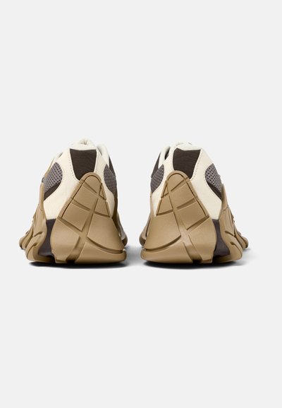 Zapatillas deportivas con una parte superior de punto cremoso ligero, acentos en marrón chocolate y una suela texturada en tono marrón claro que ofrece buen agarre. Diseño ergonómico y moldeado.