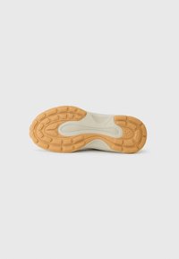 Schuhsohle mit einer strukturierten Gummisohle in Tan und Creme, die ausgeprägte Profilmuster für Grip und Flexibilität aufweist.