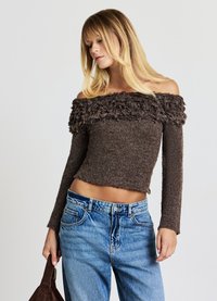 Pull marron à épaules dénudées avec un col duveteux, des manches longues ajustées et une coupe courte, associé à un jean bleu taille haute.