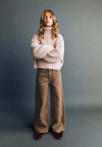 Maglione a collo alto rosa lavorato a maglia, vestibilità comoda; pantaloni beige a gamba larga con tasche laterali; scarpe slip-on bordeaux; sfondo semplice.