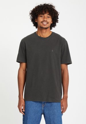 Mørk grå bomull T-skjorte med rund hals og korte ermer; har en liten logo på brystet og en avslappet passform. Brukt med blå jeans.