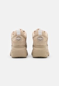 Baskets beige avec une semelle épaisse, une tige en cuir lisse, un col rembourré et un détail de logo rond sur le talon. Semelle extérieure texturée pour une meilleure adhérence.