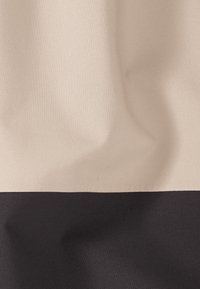 Beige en zwarte stof met zichtbare geweven textuur en zachte plooien, horizontaal verdeeld met beige bovenaan en zwart onderaan.