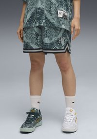 Short-sleeve teal snake-print shirt and matching shorts with black accents. One foot in green sneakers, the other in white sneakers.