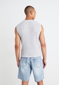 Gray, sleeveless textured top with vertical ribbing, paired with light blue denim shorts. Relaxed fit, minimalist design.