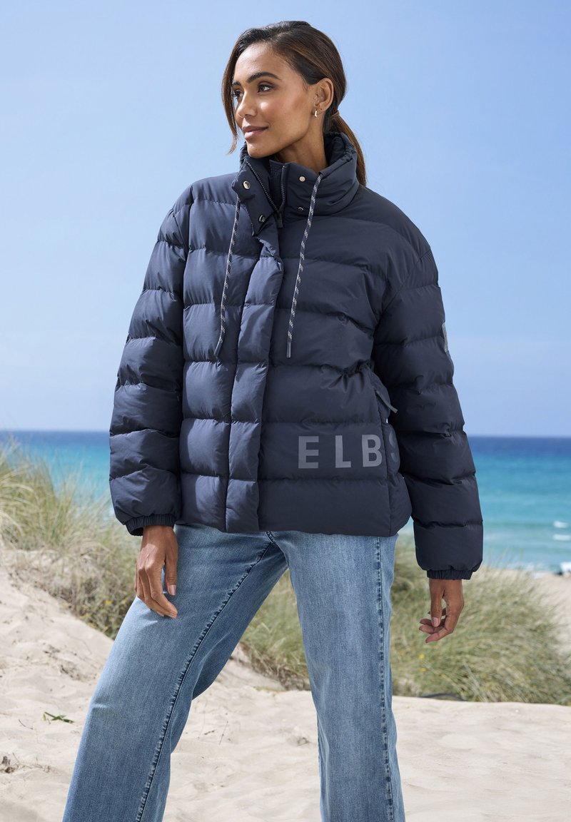Marineblaue Steppjacke mit quiltiertem Design, hohem Kragen und Kordeln. Mit der Aufschrift "ELB" auf der Vorderseite und elastischen Bündchen.
