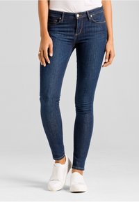 Tmavě modré skinny džíny vyrobené z denimu. Mají vysoký pas, přední kapsy a nenápadné švy. V kombinaci s bílými nazouvacími teniskami.