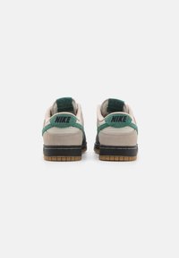 Tenisky Nike Dunk Low s béžovým semišovým svrškem, zelenými akcenty a černou gumovou podrážkou s gumovým spodkem. Dvojité značení na patách.