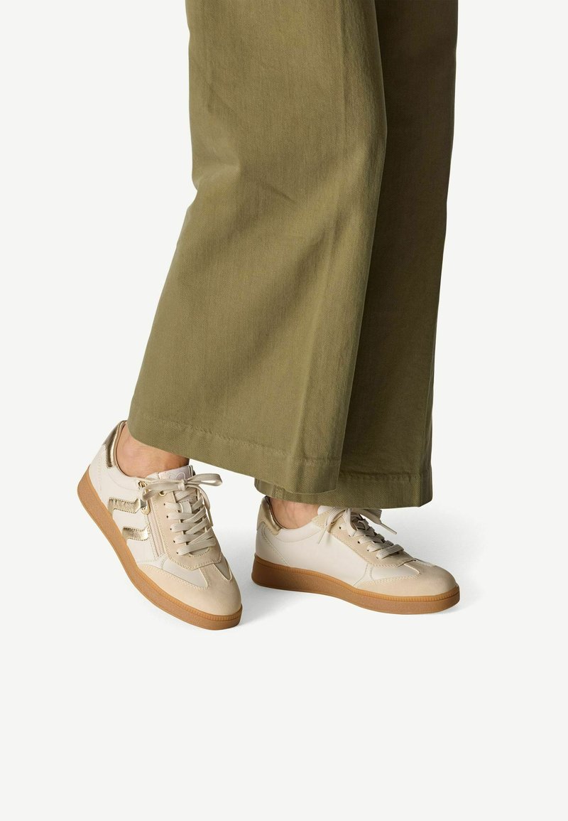 Sneakers con una parte superiore in pelle crema, dettagli testurizzati e una suola in gomma color tan. I lacci e le strisce laterali impreziosiscono il design sportivo.