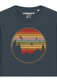 T-shirt navy avec un design circulaire composé de rayures horizontales orange, jaune et rouge, représentant une silhouette d'arbres et d'oiseaux.