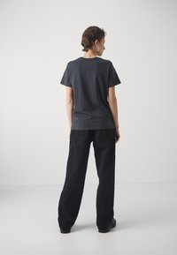 Donkergrijze katoenen t-shirt met korte mouwen en een ronde halslijn, gecombineerd met zwarte wijde broek. Eenvoudig ontwerp, geen patronen of accenten.