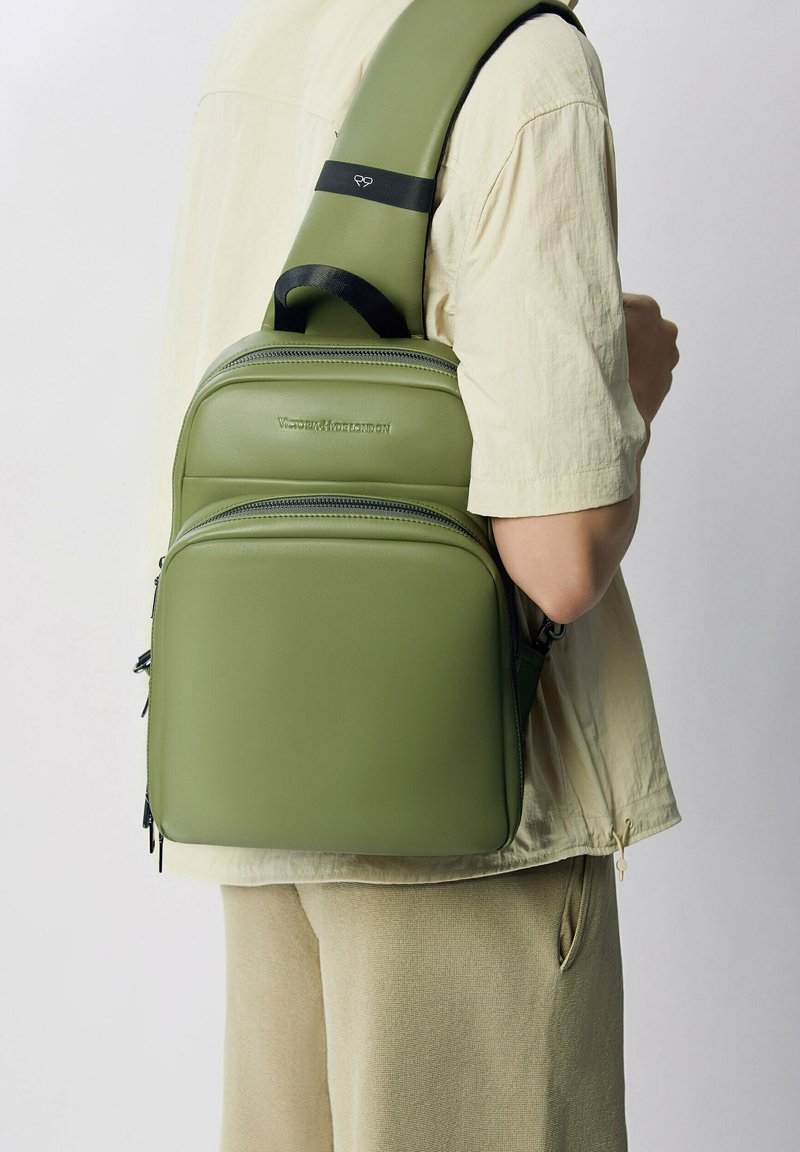 Zaino in pelle vegana verde con più compartimenti con zip, fascia regolabile e imbottita, e una finitura liscia e texture.