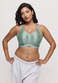 Sportbeha in muntgroen met een gestructureerd ontwerp en brede bandjes; gecombineerd met lichtgrijze joggingbroek. Voorzijde zichtbaar tegen een neutrale achtergrond.