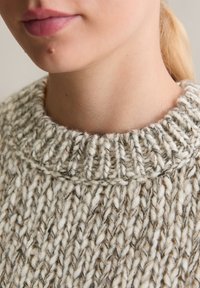 Gruba dzianinowa sweter w jasnobeżowej i off-white kolorystyce. Posiada żeberkowy okrągły dekolt oraz teksturowaną przędzę.