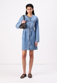 Svetlo modra denim obleka s dolgimi rokavi, gumbnim zapiranjem, dvema žepoma na prsih in pasom za vezanje. Nosi se z majhno rjavo torbico in čevlji z živalskim vzorcem.
