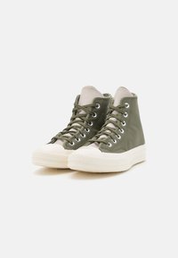Sneakers alte verdi con tomaia in pelle testurizzata, linguetta in tela grigia chiara, suola in gomma bianca e occhielli in argento per i lacci.