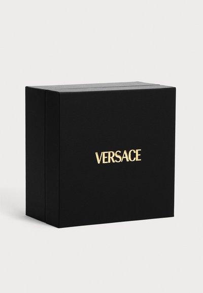 Μαύρο ορθογώνιο κουτί με χρυσό λογότυπο Versace στο κέντρο μπροστά, σε απλό ανοιχτό φόντο.