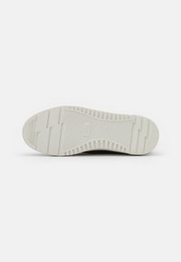 Sole of a shoe featuring a textured white rubber material with horizontal and vertical grooves. The design includes a logo imprint in the center.