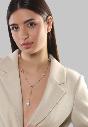 Goldene Halskette mit einer Vielzahl von Pastellperlen und einem großen, ovalen Anhänger. Getragen über einem hellbeigen Blazer mit glatter Textur.