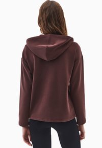 Bordowy sweatshirt z kapturem, z długimi rękawami i luźnym krojem. Miękka tkanina o gładkiej fakturze, bez widocznych wzorów i elementów metalowych.