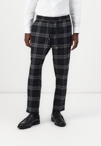 Grijze en marineblauwe geruite broek met een elastische tailleband en trekkoord. Glad materiaal met een relaxte pasvorm. Gepaard met zwarte instapschoenen.