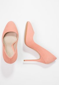 Escarpins en suède pêche avec un bout pointu et un talon stiletto fin. Ils possèdent une texture lisse et des lignes épurées, avec un logo discret à l'intérieur.