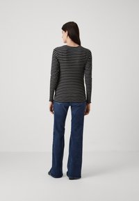 Langärmliges Oberteil mit schwarz-weißen Streifen und Rundhalsausschnitt, kombiniert mit ausgestellten blauen Jeans aus Denim, von hinten gesehen.