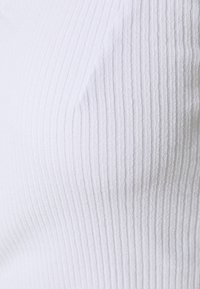 Vit ribbad strikkaprodukt med en texturerad yta, som har vertikala ränder som tillför dimension till ytan.