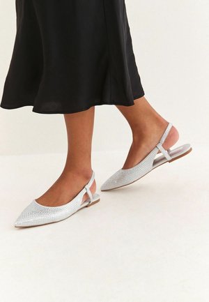 Srebrne baleriny na pasku z odkrytą piętą, z wąskim, zakończonym szpicem noskiem, teksturowaną, błyszczącą cholewką oraz płaską, brązową podeszwą. Model posiada cienki pasek wokół kostki.