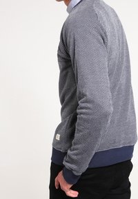 Gray textured sweater with diagonal stripes, ribbed cuffs, and a hem in navy blue. Features a small label at the lower back.