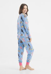 Komplet piżamowy wykonany z miękkiego materiału, z jasnoniebieskim tłem i kolorowymi bajkowymi zwierzątkami. Rękawy i dół zakończone różowymi mankietami.