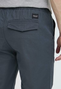 Dark blue, textured fabric pants with an elastic waistband, featuring a back pocket and a small black label.