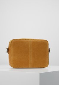 Braązowa skórzana torba na ramię z zamszu o kwadratowym kształcie, gładkiej fakturze i minimalistycznym designie. Posiada subtelne przeszycia i eleganckie zapięcie.