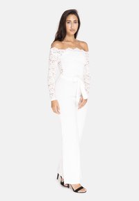 Hvid off-shoulder blondes bodysuit med lange ærmer, parret med tætsiddende hvide bukser og sorte hæle sandaler. Bundet talje accent.