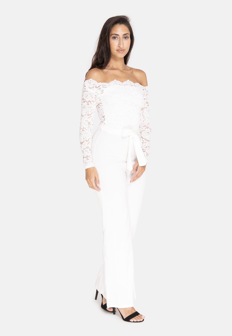 Hvid off-shoulder blondes bodysuit med lange ærmer, parret med tætsiddende hvide bukser og sorte hæle sandaler. Bundet talje accent.