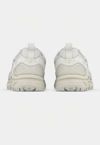 White athletic shoes with a textured upper, featuring accented panels, a rear pull tab, and a sturdy rubber sole with traction patterns.