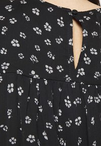 Tissu noir pour robe avec un petit motif floral blanc, avec un col en forme de trou de serrure fermé par un seul bouton noir.
