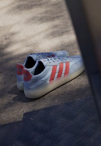 Zapatillas de color azul claro con tres rayas rojas, presentan una parte superior de cuero suave y ante, suela blanca redondeada y un acento de marca en el talón.