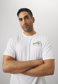 Hvid bomulds T-shirt med et grafisk motiv af en gul pickup truck og tekst på venstre bryst. Korte ærmer, afslappet pasform, glat tekstur.