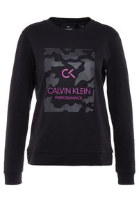 Musta huppari pitkillä hihoilla, jossa on kiiltävä maastokuvio ja pinkki "Calvin Klein Performance" -logo edessä.