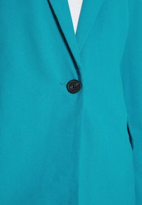 Jasně modrý blazer vyrobený z hladké tkaniny, s jedním černým knoflíkem a klasickým designem límce, se strukturovaným střihem a bez viditelného vzoru.