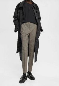 Sort quiltet lang frakke over en sort bluse, parret med gråternede bukser og skinnende sorte sko. Blød tekstur og skræddersyet design.