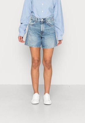 Lyseblå denim shorts med høj talje, med et lige snit, fem lomme-design og frynset kant. Parret med hvide sneakers.