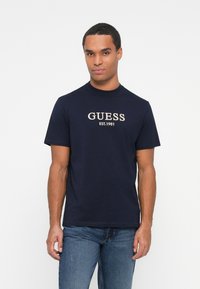 Navyblauw katoenen t-shirt met ronde hals, korte mouwen en geborduurd "GUESS EST. 1981" logo op de voorkant, met een gladde textuur.