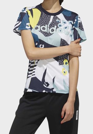 Woman wearing a short-sleeve Adidas t-shirt with abstract blue, yellow, and white patterns, paired with black Adidas pants.
