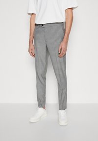 Šedé pruhované kalhoty s slim fit, které mají knoflíkový zip, poutka na pásek a jsou kombinovány s bílými teniskami. Hladká textura.