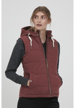 Gilet matelassé rouge avec une capuche, doté d'une fermeture éclair à l'avant, d'un cordon de serrage et de poches latérales. Porté par-dessus une chemise à manches longues grise.