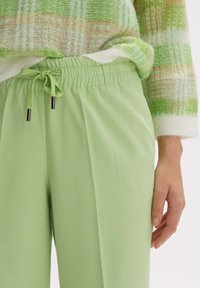 Ljusgröna elastiska byxor med dragsko i midjan, med en mjuk textur och sidofickor, i kombination med en mönstrad grön tröja.