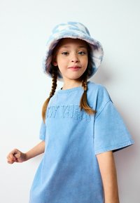 T-shirt en coton bleu clair avec "NEW YORK" brodé dans un fil assorti. Accompagné d'un chapeau seau en polaire avec un motif nuage bleu et blanc.